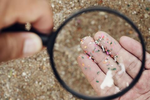 Using a magnifying glass to look at very small pieces of plastic on a beach