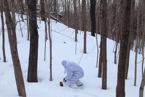 A person in a white hazmat suit collecting snow samples in a forest