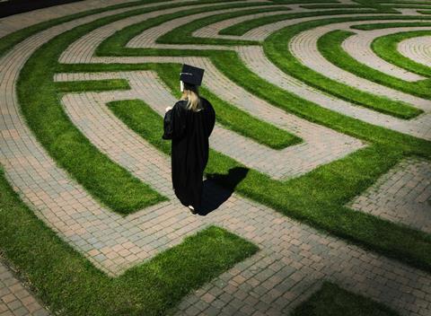 A person wearing academic clothes walking through a maze