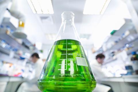 A glass conical flask of green liquid in a lab setting