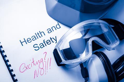 An image showing a health and safety manual on which someone scribbled 'exciting? no!). There are also safety goggles, ear defenders and the edge of a helmet visible