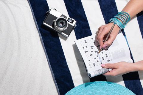 A woman doing a crossword on a beach.