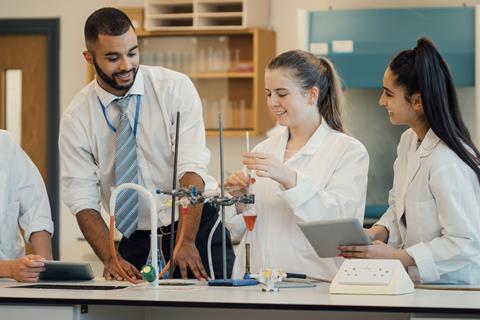 Two students talk to their teacher in a school laboratory while conducting an experiment using a pear-shaped flask