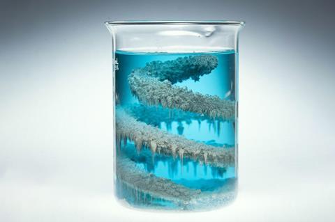 A glass scientific beaker of blue liquid with a coil of a crystalised metallic material inside
