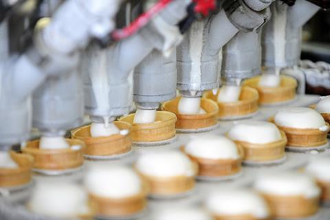 A photo of an ice cream factory machine filling a line of cones with ice cream