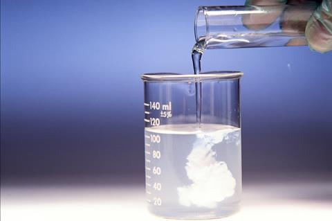 A photo of a test tube of liquid being poured into a beaker of another liquid and a white precipitate forming