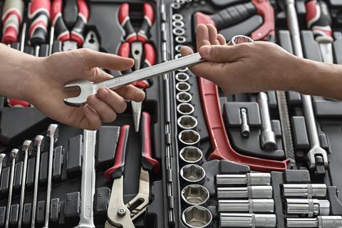 One person handing a spanner to another, toolkit in background