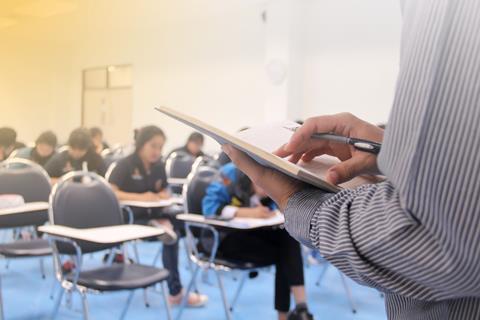 A teacher supervising students taking an exam with some empty seats