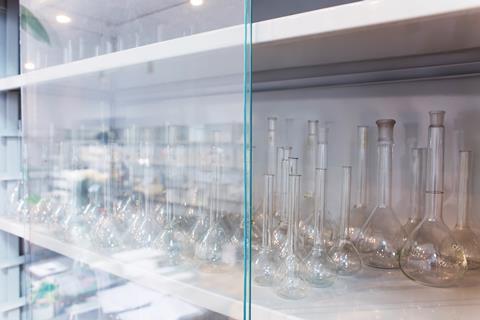 An image showing chemistry flasks of different size put away on shelves in a glass fronted cupboard