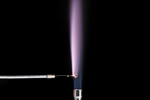 A purplish flame coming from burning a small amount of liquid over a bunsen burner