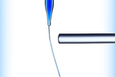 A glass rod bends a small vertical stream of blue water