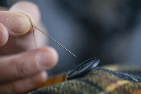 An image showing the mending of a coat by sewing a button back in place