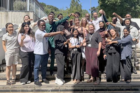 An outdoor group photo of a range of new teachers pointing to their trainer - Eleanor Mortimer