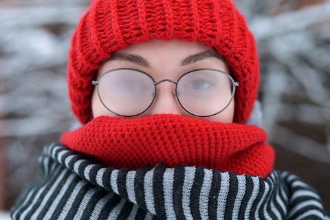 A woman wrapped up in a wooly hat and scarf with fogged up glasses