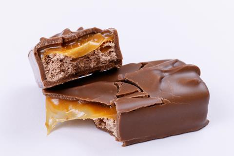 A chocolate bar broken in two with layers of caramel and light brown milk cream visible