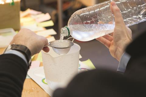 A photograph of a teacher demonstrating an experiment with water and hydrogels