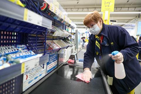 An image showing an employee in a face mask sanitizing surfaces by a cash desk in a Metro Cash and Carry store