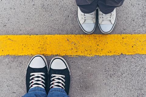 Two pairs of feet either side of a painted, yellow line on the ground