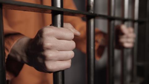 A man holding the bars of a jail cell