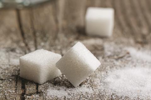 Three sugar cubes on a wooden surface surrounded by sugar granules