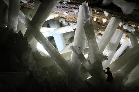Enormous gypsum crystals in a Naica cavern, found during mining; the silhouette of a miner in the bottom right provides scale