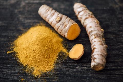 Turmeric roots and orange turmeric powder on a dark grey wooden surface