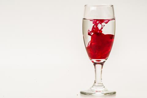 Red food colouring diffusing in a glass of water against a light background