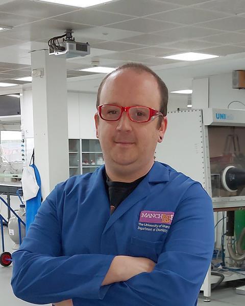 A man in a blue lab coat with red glasses in a modern laboratory