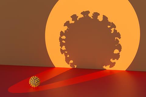 A spotlight on a small covid virus casting a large silhouette on a wall