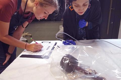 A photo of museum conservators checking the oxygen levels of rubber objects stored inside anoxic enclosures