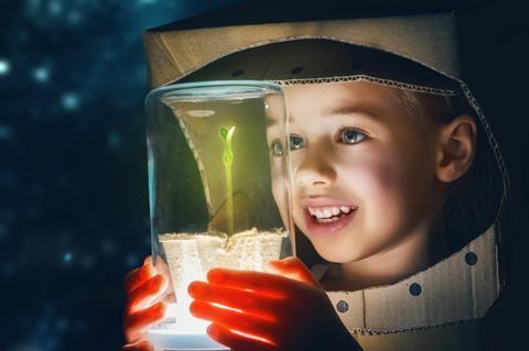 Child in a spacesuit looking at a plant