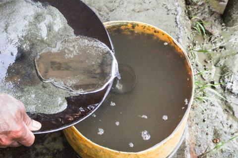 A small scale gold miner pours mercury from their prospecting pan into a tub of water