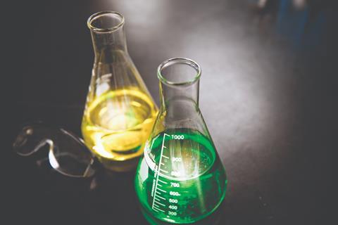 A photo of a yellow sollution in one conical flask and a green solution in another