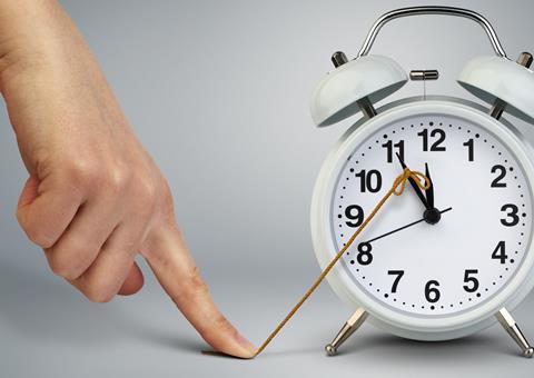 A forefinger holds down a string attached to the big hand of an alarm clock, effectively stopping time