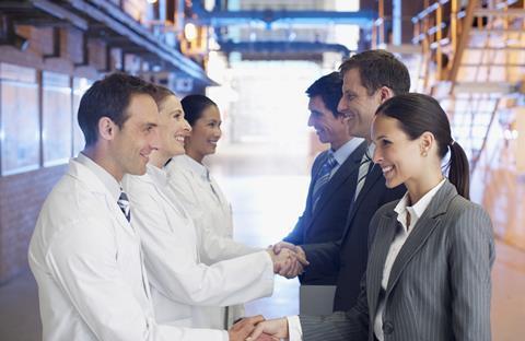 Three people in suits shaking hands with three people in lab coats