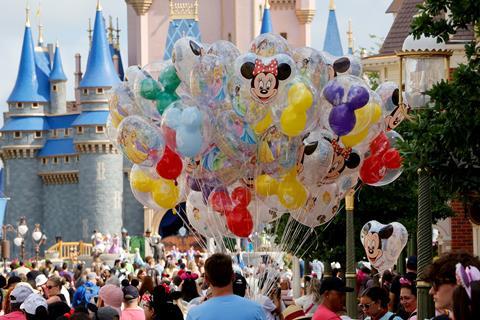 A vendor selling balloons in a crowd with the Disney World's Magic Castle behind