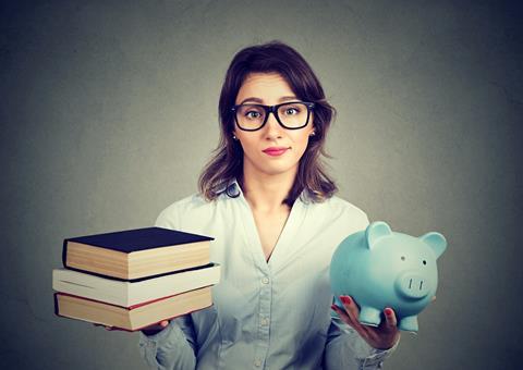 Young woman with glasses, books in one hand, piggy bank in other, pained expression