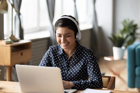 Woman wearing headphones smiles at the laptop she's working on