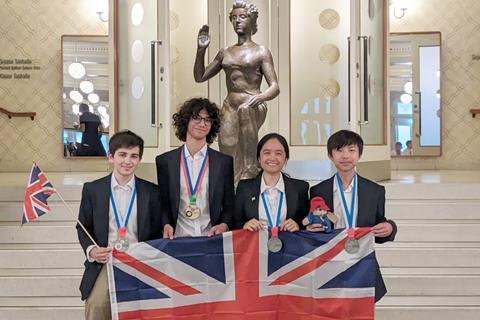 A group of four students wearing medals and holding a Union Jack flag