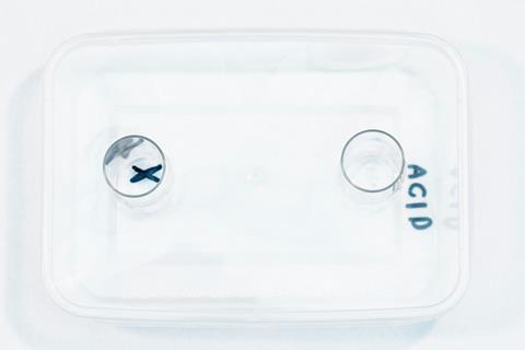 A clear plastic tile with two wells on. One is labelled Acid and the other has a cross drawn under it.