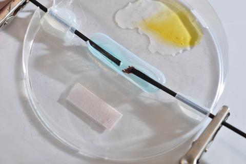 A petri dish with a drop of yellow liquid, a piece of paper and a drop of blue liquid hooked up to electrodes