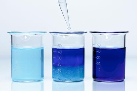 Three glass beakers. The one on the left holds a light blue liquid. The one in the middle has a dropper adding clear liquid and the blue liquid is a little darker with a precipate at the bottom. The right beaker holds a dark blue liquid.