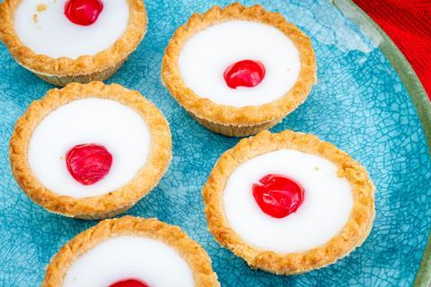 Pastry tarts with white icing and a red cherry on a blue plate