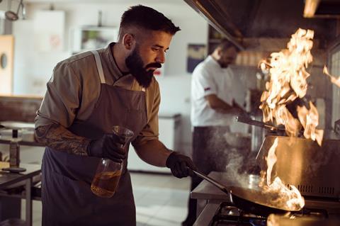 A photo of a chef in a kitchen using a flambé technique