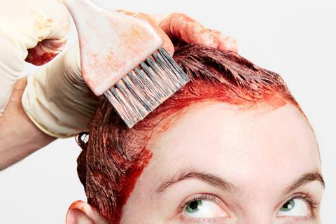 Red hair dye being applied to a woman's hair with a brush
