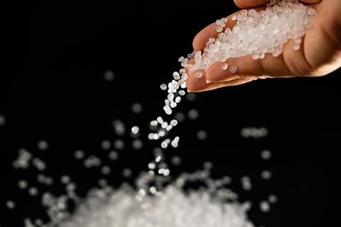 Colourless plastic pellets  fall from a hand against a black background