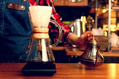 Glass coffee jar with filter paper and hand holding old-fashioned metal kettle of water