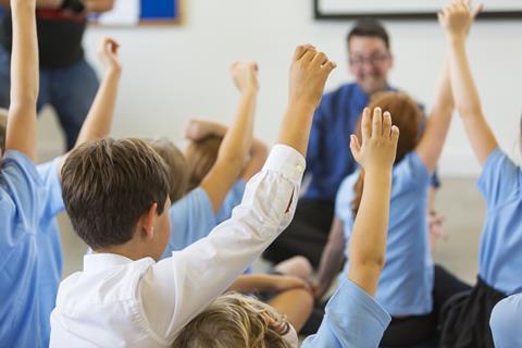 Pupils sitting on the floor around a teacher with their hands up