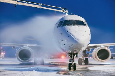 A plane on some tarmac both covered with ice. A crane is spraying the plane and the ice is melting.