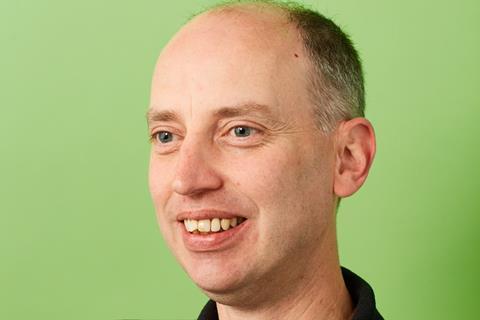 Side view of Andrew Hallett smiling with a green background.